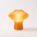 NAMU mid century fluted table lamp in amber, lit, on a plain light background