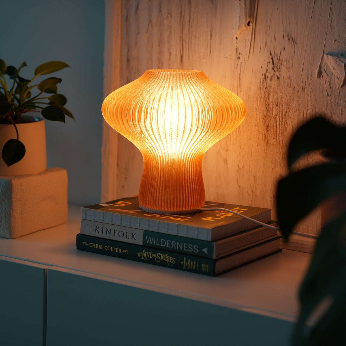 NAMU amber lamp glowing on a stack of books beside a potted plant